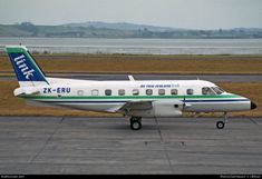 a small white and green airplane on the tarmac at an airport with water in the background