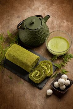 a green teapot and some white mushrooms on a wooden table next to a towel