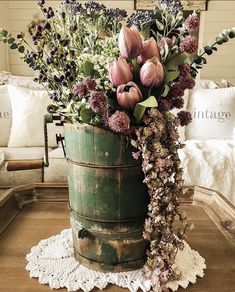 a green bucket filled with lots of flowers on top of a wooden table next to a couch