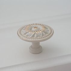 a white cabinet knob with an ornate design on the top and bottom, sitting on a white surface