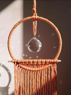 an orange dream catcher with a crystal hanging from it's center and sun shining through the window