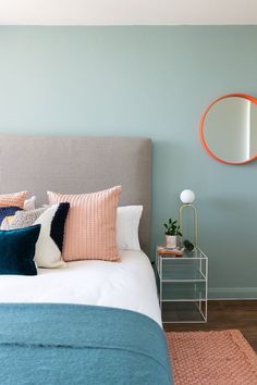 a bed with blue and pink pillows in a bedroom next to a round mirror on the wall