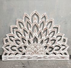 an intricately designed wooden piece on the ground in front of a gray wall and concrete floor