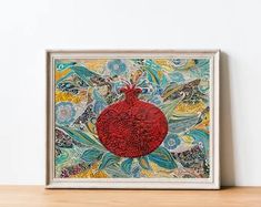 a painting is displayed on a shelf in front of a white wall with a red pomegranate