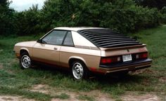 a tan car parked on top of a grass covered field next to trees and bushes