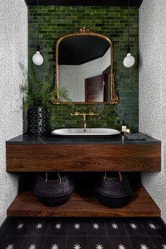 a bathroom with green brick walls and black tile flooring, an oval mirror above the sink