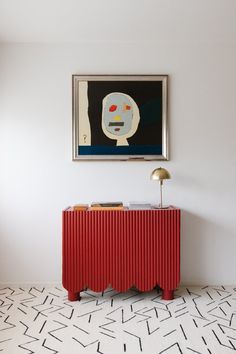 a painting hangs above a red cabinet in a white room