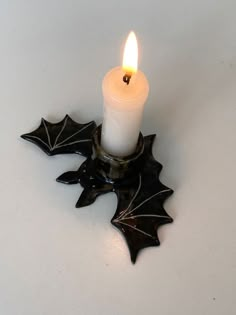 a lit candle sitting on top of a black holly leaf decoration with a white background