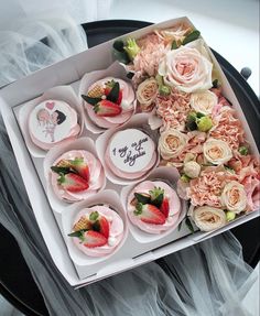 a box filled with lots of cupcakes covered in pink frosting and topped with strawberries