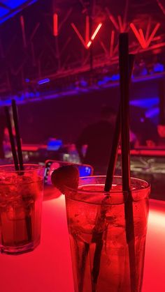 two glasses filled with drinks sitting on top of a table in front of a red light