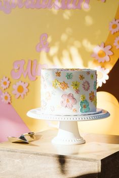 a white cake sitting on top of a table next to a yellow and pink wall