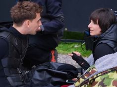 a man and woman sitting on the ground talking to each other with backpacks behind them