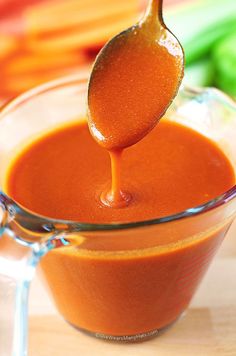 a spoon full of sauce being poured into a glass container