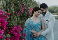 a man and woman standing next to each other in front of flowers