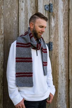 a man with a beard wearing a gray and red striped scarf standing in front of a wooden door