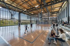 people are playing basketball in an indoor court with wooden floors and large windows on the wall