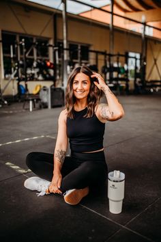 a woman sitting on the ground with her hands behind her head, smiling at the camera