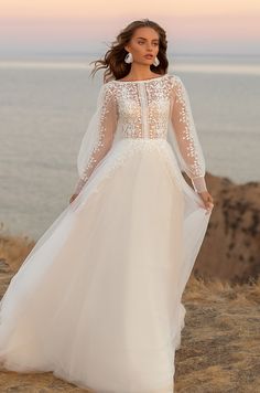 a woman in a white wedding dress standing on top of a hill next to the ocean