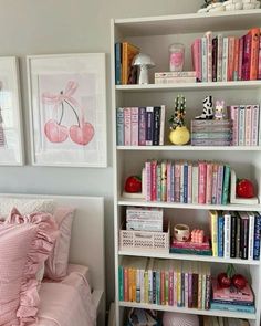 a white book shelf filled with lots of books next to a pink bed and pillows