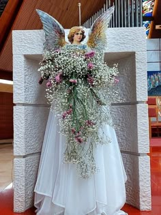 a white statue with flowers and angel wings on it's head in front of a wall