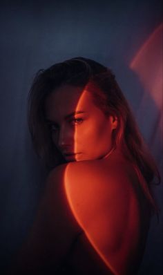 a woman with red light on her chest and shoulder, in the dark room next to a wall