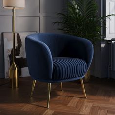 a blue chair sitting on top of a hard wood floor next to a lamp and potted plant