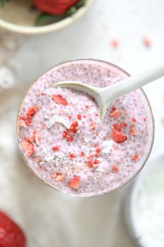 a smoothie in a glass with strawberries on the side and a spoon sticking out