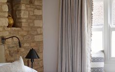 a bedroom with a stone wall and white bedding, two lamps on either side of the window