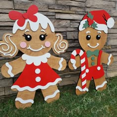 two wooden gingerbread man and woman standing next to each other in front of a brick wall