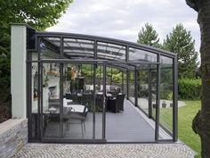 a glass enclosed patio with table and chairs in the back ground, surrounded by trees