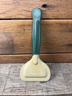 a green and white spatula sitting on top of a wooden table next to a wall