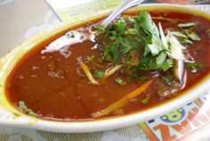 a bowl filled with soup and garnish on top of a table next to a book