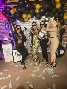 three women pose for a photo in front of a backdrop with money notes and balloons