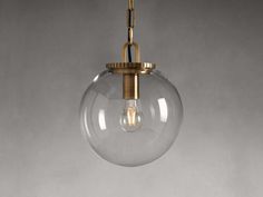 a clear glass globe light hanging from a brass chain