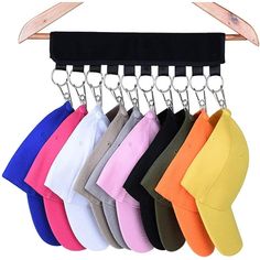 six baseball caps hanging on a rack with metal hooks and clippings, all in different colors