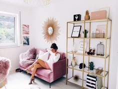 a woman sitting on a pink couch in front of a wall with pictures and decor