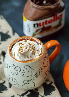 there is a mug with whipped cream in it and an orange on the table next to it