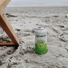 a can of soda sitting in the sand next to a wooden chair on the beach