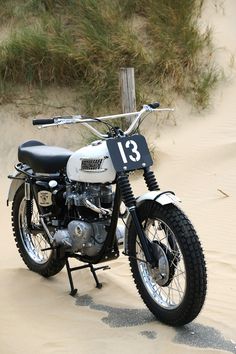 a motorcycle parked on top of a sandy beach next to grass and sand dunes in the background