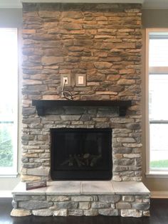 a stone fireplace with two windows in the background