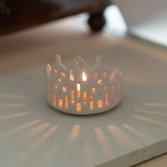 a lit candle sits on top of a white table with a shadow cast on it