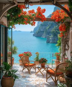 an outdoor patio with potted plants and flowers on the table next to it, overlooking the ocean