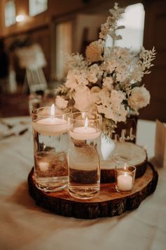 candles are lit on a wood slice with flowers in the background at a wedding reception