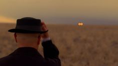 a man in a black hat looking at the sky with an orange dot on it