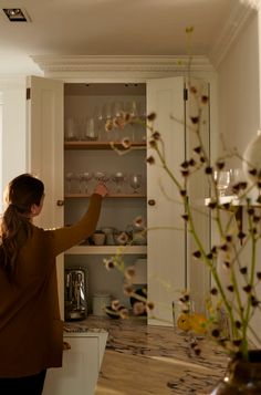 a woman standing in front of a cabinet filled with wine glasses and other things on it