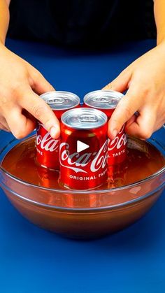 two hands grabbing cans of coca - cola out of a bowl on a blue surface