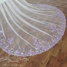 wedding veil with purple flowers on it sitting on the floor in front of a wooden floor