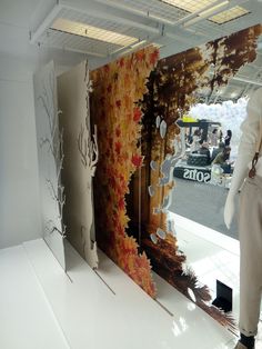 a mannequin is standing in front of a wall with autumn leaves on it