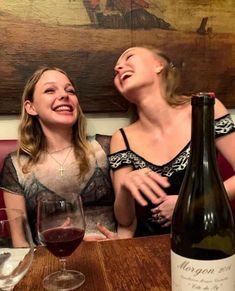 two women are sitting at a table with wine glasses and bottles in front of them