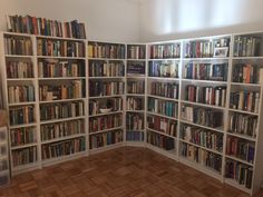 a room filled with lots of books on top of white shelving unit units next to a wooden floor